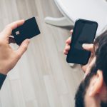 Pessoa segura um celular e um cartão de crédito durante um pagamento digital.