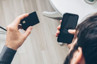 Pessoa segura um celular e um cartão de crédito durante um pagamento digital.