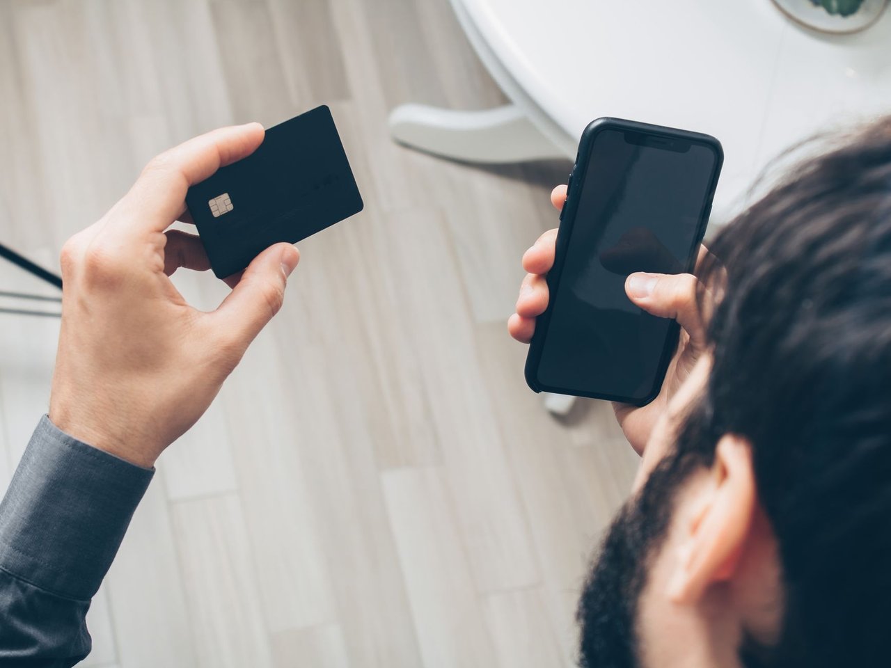 Pessoa segura um celular e um cartão de crédito durante um pagamento digital.