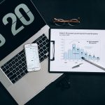 Vista superior de uma mesa com laptop, smartphone e gráficos de análise financeira.