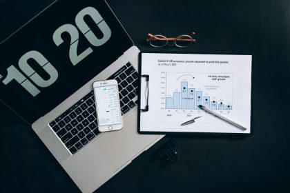 Vista superior de uma mesa com laptop, smartphone e gráficos de análise financeira.