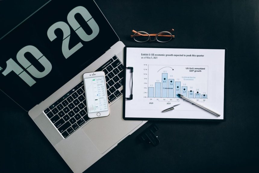 Vista superior de uma mesa com laptop, smartphone e gráficos de análise financeira.