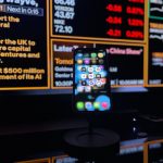 Smartphone com aplicativos de inteligência artificial diante de uma tela com dados financeiros.