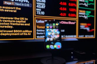 Smartphone com aplicativos de inteligência artificial diante de uma tela com dados financeiros.