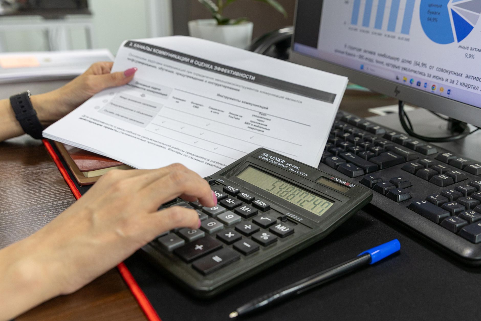 Pessoa calcula dados financeiros com uma calculadora e documentos sobre uma mesa de escritório.